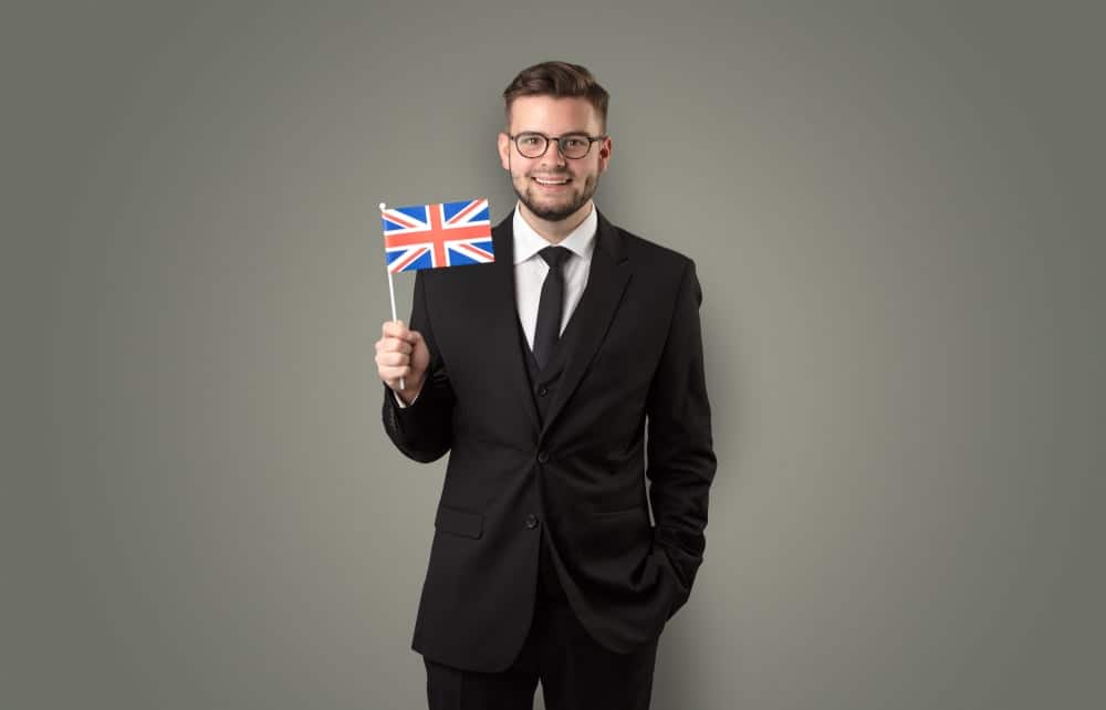 Cheerful student standing in front of wall with national flag on his hand